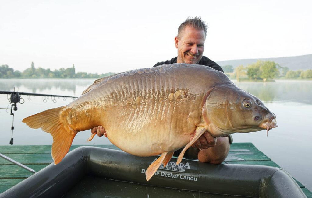 das bild zeigt frank schmidt mit einem großen karpfen und einer anaconda abhakmatte, gefangen mit einem boilie