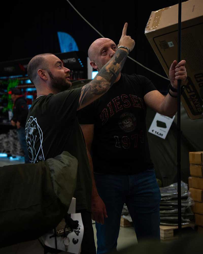 Angler vergleichen eine Karpfenrute und weiteres Angelzubehör am Messestand