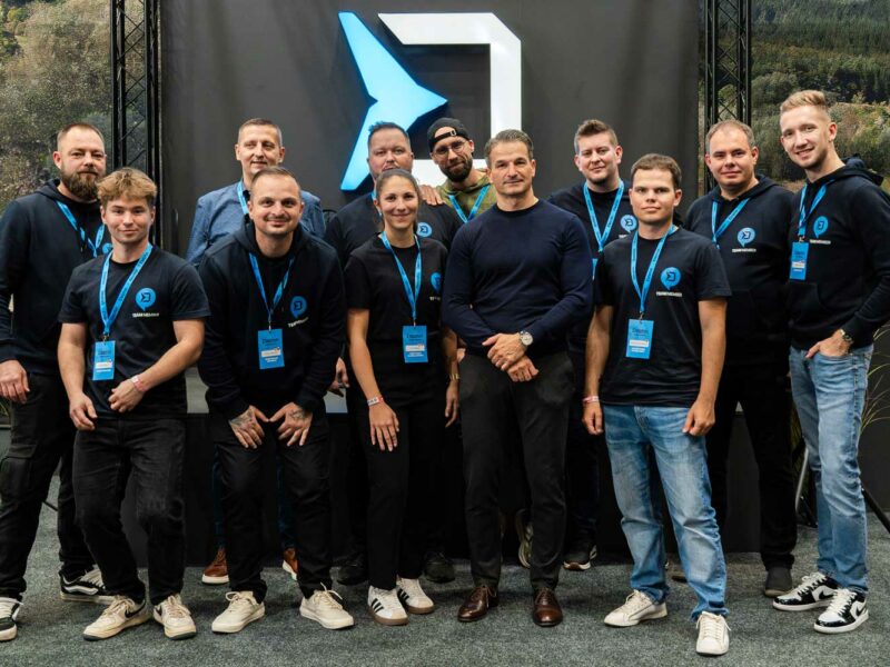 Delphin Fishing Team in dunkelblauer Delphin-Kleidung vor der großen Delphin-Logowand am Messestand