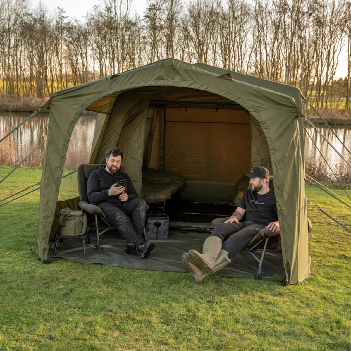 Zwei Angler sitzen unter einem geöffneten Avid-Carp-InflataHouse am See