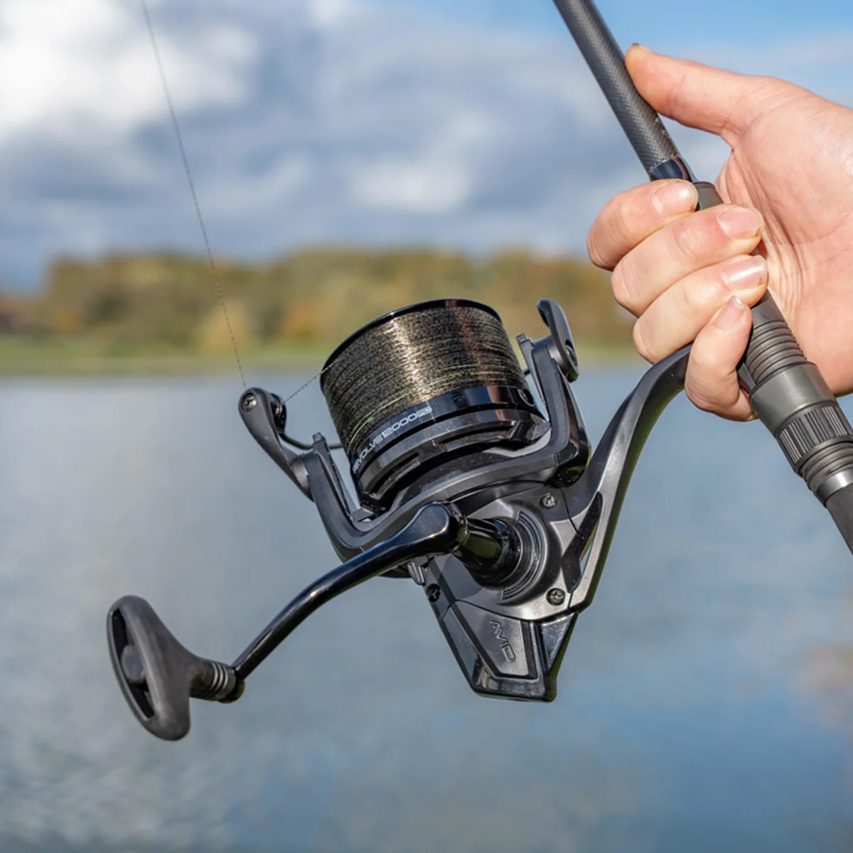 Avid-Carp-Revolve-12000FD-Karpfenrolle an einer Rute vor einem Gewässer