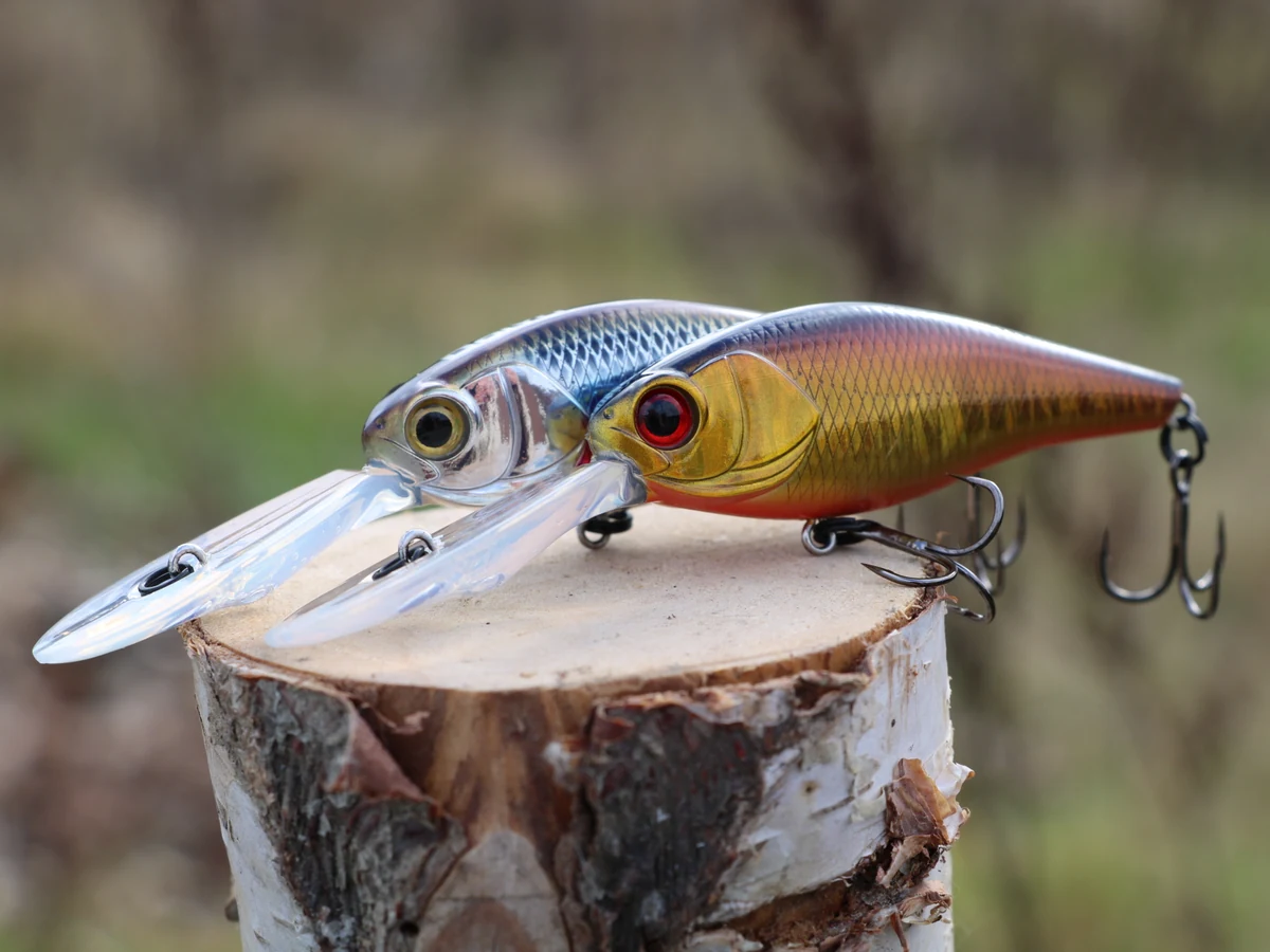 Zwei Hardbaits mit Drillingen auf einer Holzoberfläche