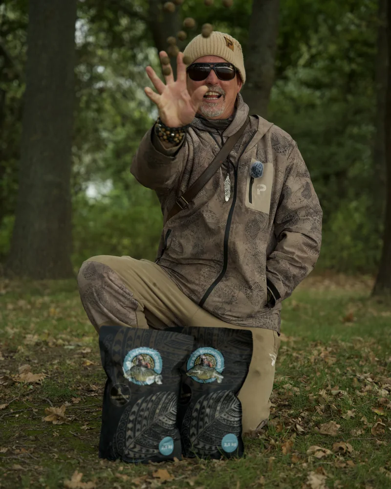 Angler wirft Boilies in die Luft; vor ihm stehen zwei Beutel Pykas Fischfudder.
