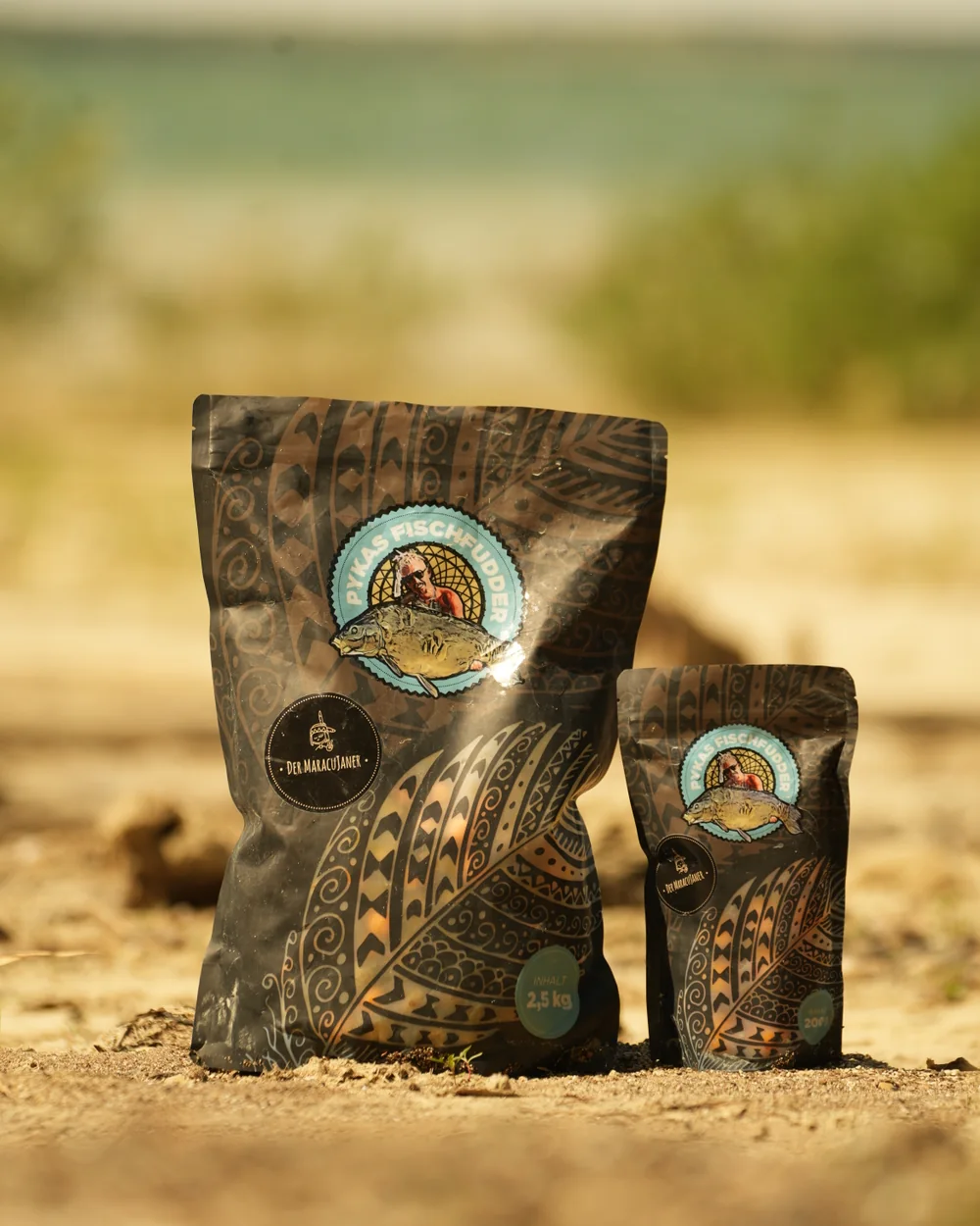 Two bags of Der Maracujaner by Pykas Fischfudder on sandy ground.