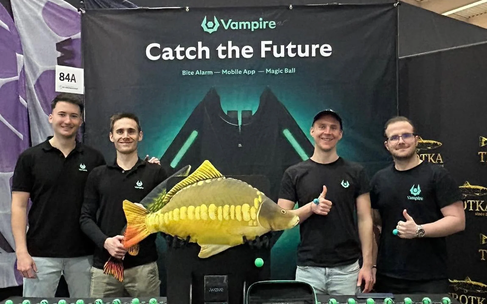 Vier Männer am Vampire-Messestand mit Karpfenmodell und Markenbanner